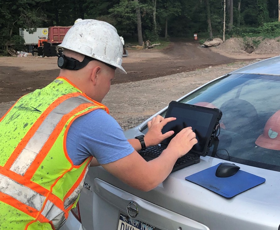 A photograph of a NYSDOT worker using a tablet in the field.